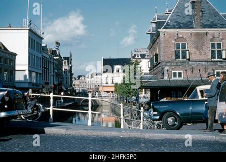 A view looking east from the canal bridge – the Waagplein crossing – in the centre of Leeuwarden, Friesland, the Netherlands in c.1960. The city is the provincial capital and seat of the Provincial Council of Friesland. It is the main economic hub of Friesland and is a former royal residence and has a city centre with many historic buildings – a vintage 1950s/1960s photograph. Stock Photo