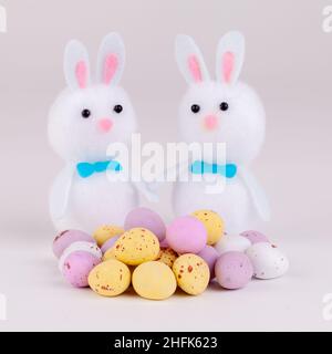 Easter bunnies with candy covered chocolate easter eggs on a plain grey background