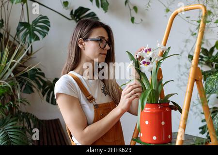 Gardening as healthy hobby. Young woman working in home garden, taking care about orchid flower Stock Photo