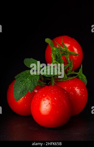 Ripe organic tomatoes on the black table in low key with water drops Stock Photo