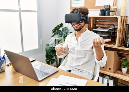 Young arab man using vr goggles doing guitar gesture at office Stock Photo