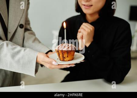 Close up of colleagues bringing Birthday cake to young woman in office, focus on cupcake with candle Stock Photo