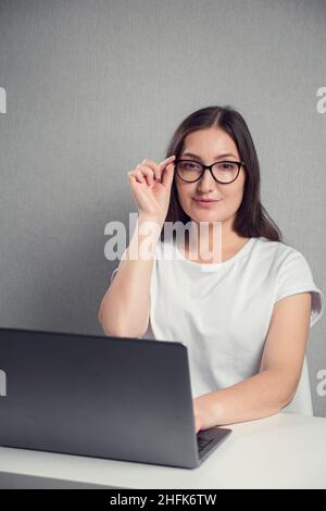 young brunette woman in glasses sitting in front of laptop, copy space Stock Photo