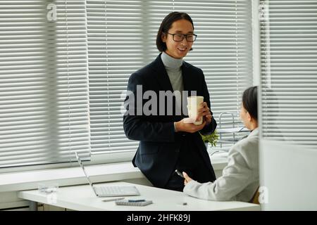 Portrait of smiling Asian businessman talking to female colleague in office during coffee break, copy space Stock Photo