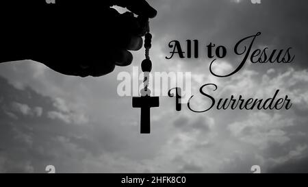 Christianity inspirational message - All to Jesus I surrender. With hand holding Rosary and sky background. Stock Photo