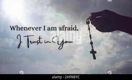 Christianity inspirational quote - Whenever I am afraid, I trust in You. With hand holding Rosary with sky background. Stock Photo