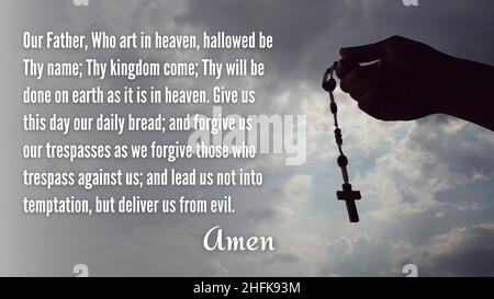 Christian prayer of Our Father with hand holding Rosary and sky background. Christianity concept. Stock Photo