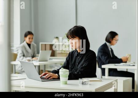 Side view portrait of young Asian woman looking at laptop screen while working in office Stock Photo