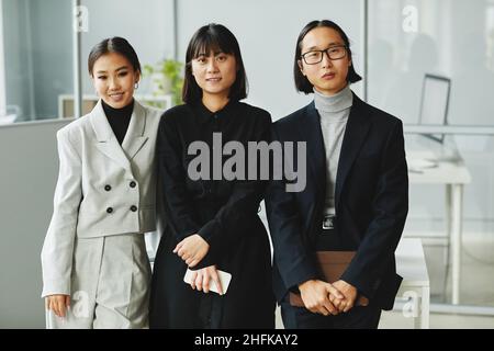 Waist up portrait of three Asian business people looking at camera while standing in office Stock Photo