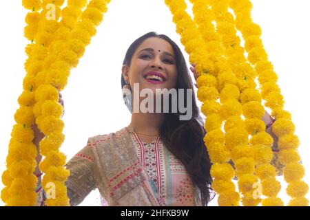 A woman dressed in traditional wear standing amidst festive flower garlands decoration. Stock Photo