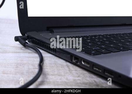 Laptop, computer is charging from a 220-volt outlet on a desk near the wall. Energy, accumulation Stock Photo