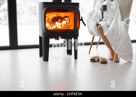 Woman sitting on chair by the burning fireplace at home Stock Photo