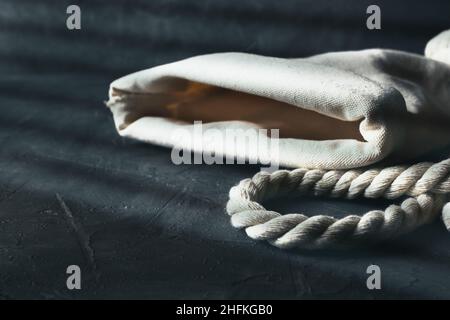 Old sack with rope in dark mood shot with warm window light. Background with copy space. Stock Photo