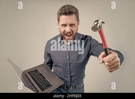 Failed to complete a task. Angry man shout holding hammer and laptop ...