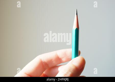 Green graphite pencil in human hand. White wall background. Stock Photo