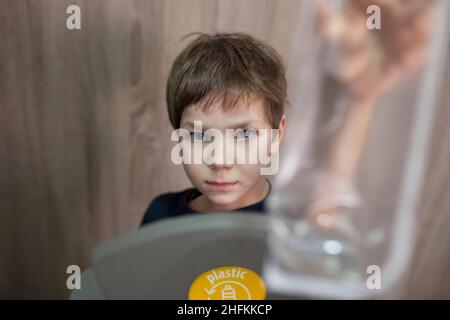 Child boy throwing soft food container to waste bin for plastic at home. Education about Waste Segregation concept Stock Photo