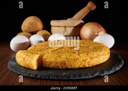 A closeup of a fresh tasty Spanish omelette and the ingredients on the background, a traditional dish from Spain Stock Photo
