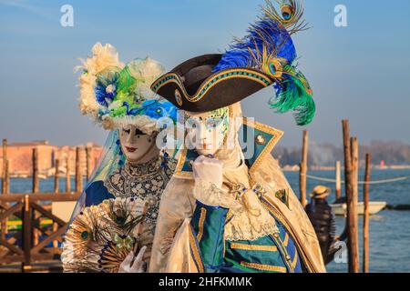 Two participants in colourful historic Venetian fancy dress costumes pose by the lagoon, Venice Carnival, Carnevale di Venezia, Italy Stock Photo