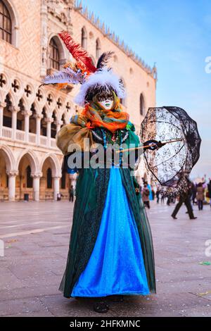 Woman in colourful historic Venetian fancy dress costume, hat and mask, poses at Venice Carnival, Carnevale di Venezia, Italy Stock Photo