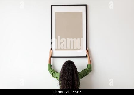 Unrecognizable Female Hanging Blank Poster In Frame On Wall Indoor Stock Photo