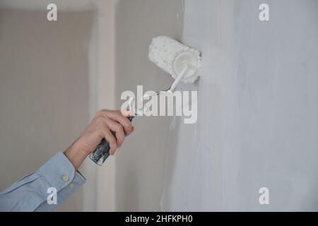 Close-up of mans hand using paint roller with white paint. Stock Photo