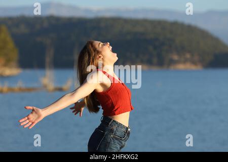 Excited woman in red screaming to the air outstretching arms in a lake a sunny day Stock Photo