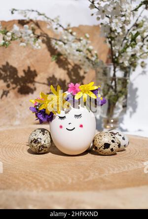 beautiful egg is decorated with a wreath of fresh flowers and a painted cute face with a smile and closed eyes. creative ideas for decor. happy easter Stock Photo