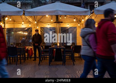 A waiter stands in an empty restaurant terrace as tourists pass by in the Ramblas of Barcelona, Spain on January 15, 2022. The hospitality and tourism industries have again been hit by the spread of the new Omicron variant of Covid-19. (Photo by Davide Bonaldo/Sipa USA) Stock Photo