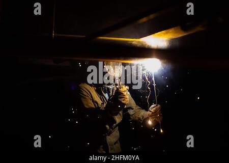 Welding of metal. Worker in mask and gloves. Bright light and sparks. Black background. Stock Photo