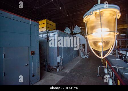 Karagandy, Kazakhstan - June 08, 2012: Machine room of heat power station. Grey generator machine left. Emergency lamp (right) is out of focus. Stock Photo