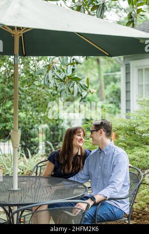 Acouple of a husband and wife sitting under a shaded umbrella patio table outside in the backyard Stock Photo