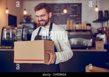 Joyful male worker with parcel standing in coffee shop Stock Photo