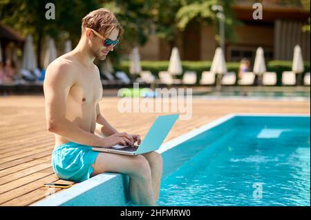 Young man at the swimming pool working on a laptop Stock Photo