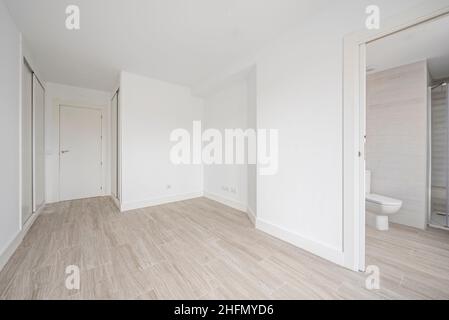 Empty room with white fitted wardrobes, white walls and wood-like ceramic tile floors and en-suite bathroom Stock Photo
