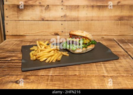 Beef burger with tomatoes and pumpkin seeds, melted cheese and lamb's lettuce garnished with french fries Stock Photo