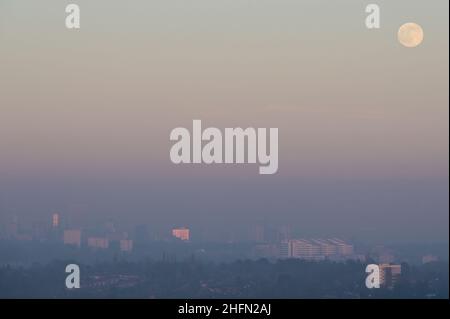 Frankley, Birmingham, UK. 17th Jan, 2022. The first full moon of 2022 called the Wolf Moon, rises above Birmingham which is surrounded by thick haze blocking much of its view from the hills of Frankley, West Midlands. The large white building of Queen Elizabeth Hospital in Selly Oak is just visible below the moon. Pic by Credit: Stop Press Media/Alamy Live News Stock Photo