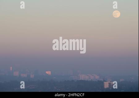 Frankley, Birmingham, UK. 17th Jan, 2022. The first full moon of 2022 called the Wolf Moon, rises above Birmingham which is surrounded by thick haze blocking much of its view from the hills of Frankley, West Midlands. The large white building of Queen Elizabeth Hospital in Selly Oak is just visible below the moon. Pic by Credit: Stop Press Media/Alamy Live News Stock Photo