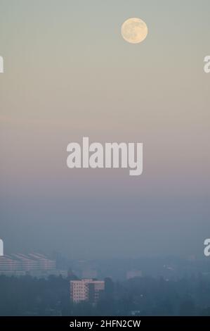 Frankley, Birmingham, UK. 17th Jan, 2022. The first full moon of 2022 called the Wolf Moon, rises above Birmingham which is surrounded by thick haze blocking much of its view from the hills of Frankley, West Midlands. The large white building of Queen Elizabeth Hospital in Selly Oak is just visible below the moon. Pic by Credit: Stop Press Media/Alamy Live News Stock Photo