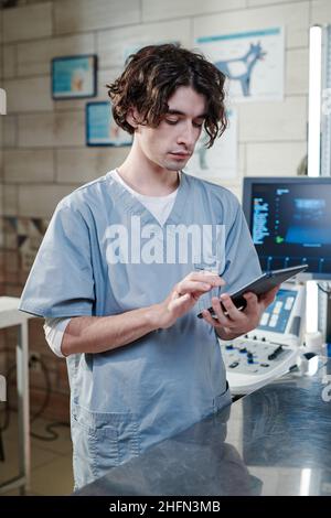 Serious doctor concentrating on his online work, he typing on digital tablet while standing at medical clinic Stock Photo