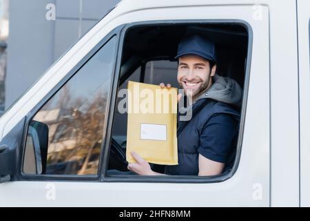 Smiling courier holding parcel and looking at camera in car Stock Photo