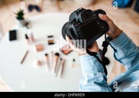 Object Photography. Unrecognizable Female Photographer Taking Photo Of Cosmetic Products On Desktop, Closeup Of Hands Holding Camera Indoors. Cropped, Stock Photo