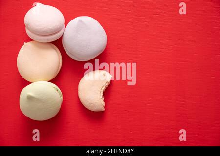 Round multi-colored marshmallows in a pile and one bitten half of a marshmallow on a red background, top view copy space. Delicious sweets and food ba Stock Photo