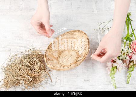 Florist at work: How to make easter floral table decoration with pink roses, matthiolas and ranunculus flowers in wicker basket. Step by step, tutoria Stock Photo