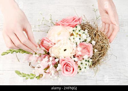 Florist at work: How to make easter floral table decoration with pink roses, matthiolas and ranunculus flowers in wicker basket. Step by step, tutoria Stock Photo