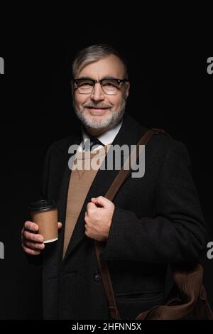 positive bearded man with leather bag and glass of whiskey looking at camera isolated on black Stock Photo