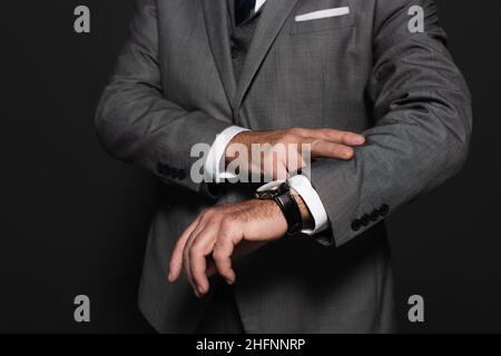 partial view of man in formal wear checking time on wristwatch isolated on dark grey Stock Photo