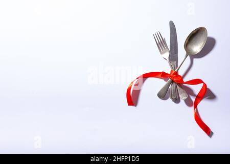 Overhead view of cutlery tied tightly with red ribbon with copy space on white background Stock Photo