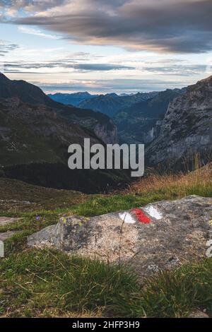 Lauterbrunnen Valley - View out over the valley during sunset. From the Schmadrihütte, in the foreground a stone with red and white hiking markings. Stock Photo