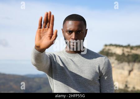 Front view portrait of an angry man with black skin gesturing stop in the mountain Stock Photo