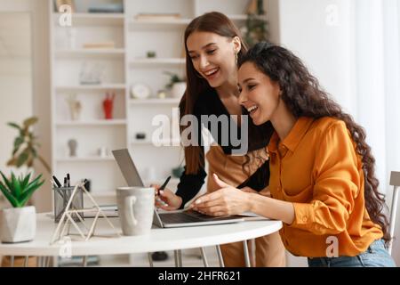 Two Happy Ladies Using Laptop Computer Working Online In Office Stock Photo
